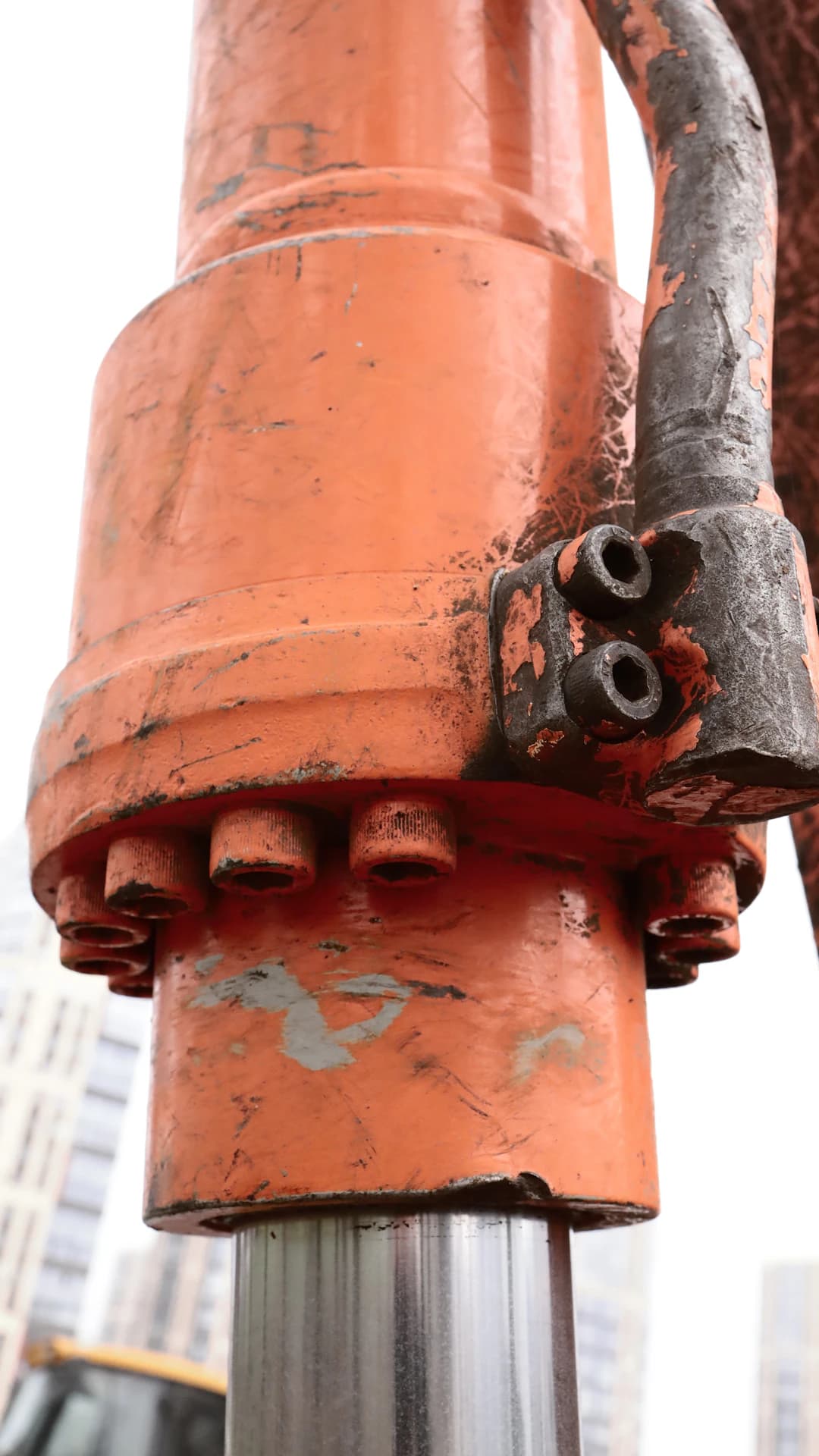 Close-up of an orange hydraulic cylinder with heavy-duty bolts during a workshop rebuild
